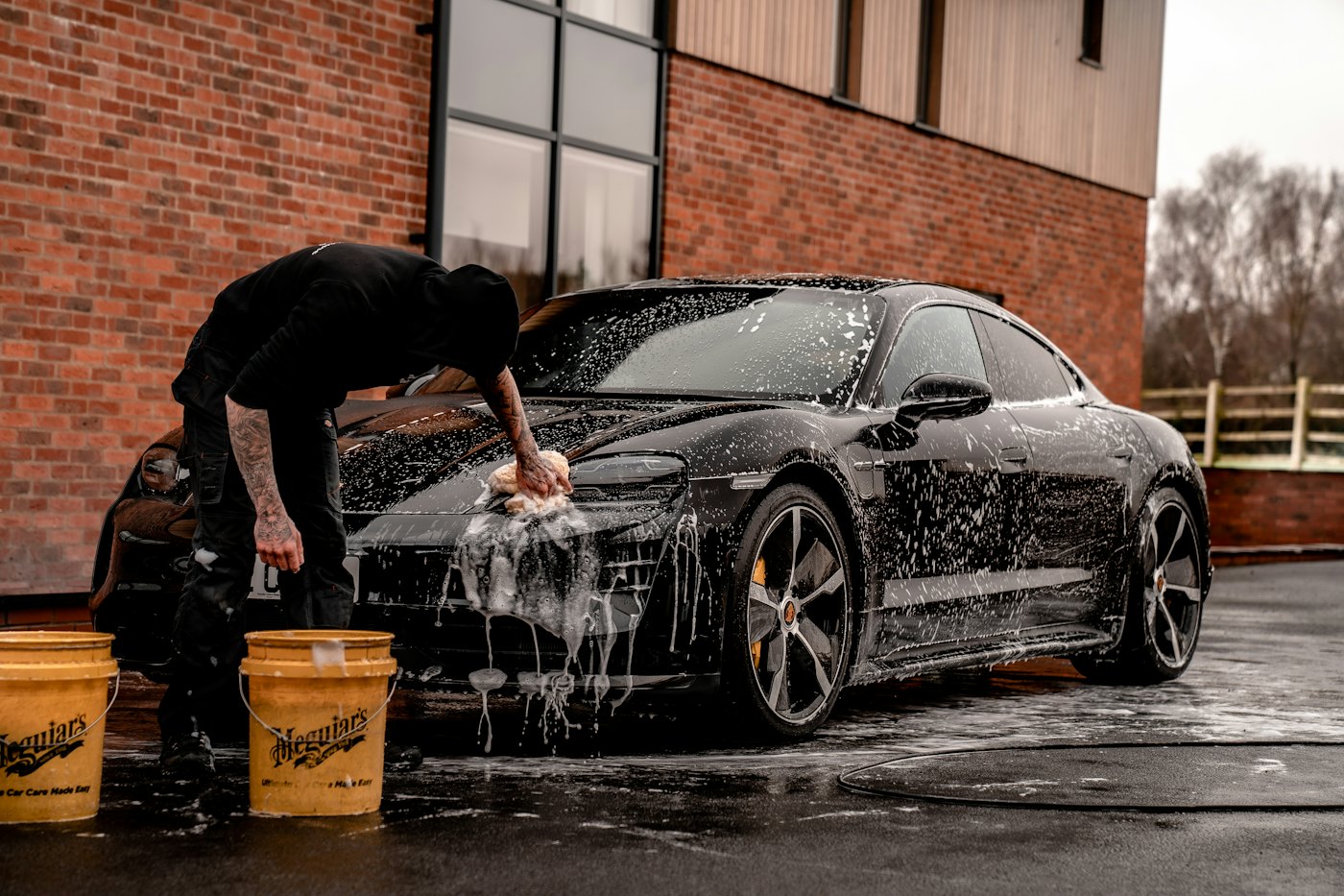 Detailer hand-washing a black car outside the studio